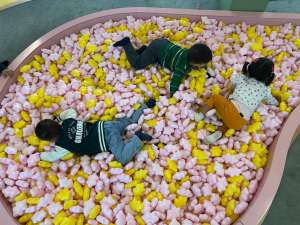 Niños acostados sobre una piscina de pelotas rosadas y amarillas